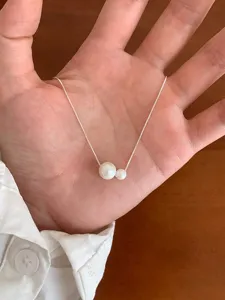 Gros plan d'un collier chaîne en argent fin avec deux perles blanches dans la main.