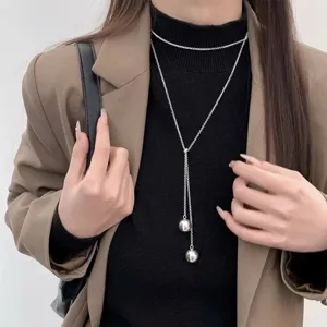 Dettaglio di una collana lunga in argento minimalista a doppia sfera, elegante gioiello da maglione.
