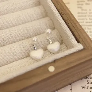 Close-up detail of S925 silver brushed heart pearl earrings in a wooden jewelry box.