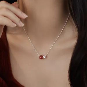 Detail shot of a delicate S925 silver necklace featuring a red agate bead and small silver pendant.