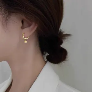 Gros plan détail de boucles d'oreilles créoles dorées S925 minimalistes avec petit pendentif carré.