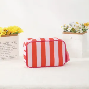Close-up of pink and red striped cosmetic bag with tassel, soft white textured background.