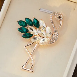 Broche flamand rose exquise avec strass verts et transparents sur metal dore et elegant.