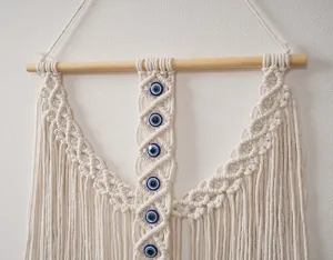 Tenture murale en macramé tissée à la main style bohème avec perles œil bleu et pompons.