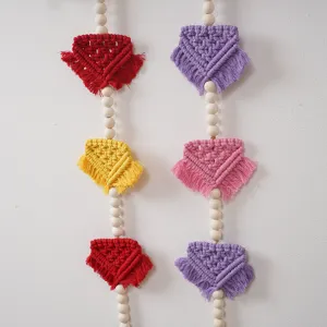Macrame wall hanging detail showcasing vibrant woven triangle flags and natural wooden beads.