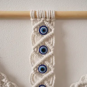 Détail de tenture murale macramé bohème avec perles œil et bâton en bois naturel.