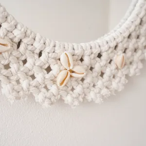 Close-up detail of handmade macrame mirror woven with white cotton rope and natural seashells.