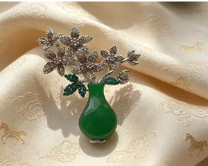 Detailed shot of a vintage green jade vase brooch with shimmering rhinestones and orchid flowers.