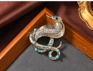Vintage cobra brooch with simulated turquoise and clear rhinestones, elegant gold tone fashion pin.