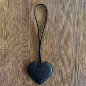 Vista detallada del dije de bolso en forma de corazón de cuero PU negro con textura y tira.