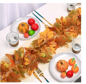 Detailed view of autumn artificial maple leaf vine with mini pumpkins on a white table