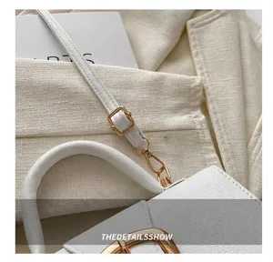 Detailansicht der verstellbaren Goldschnalle und des weißen Riemens einer kleinen Tasche