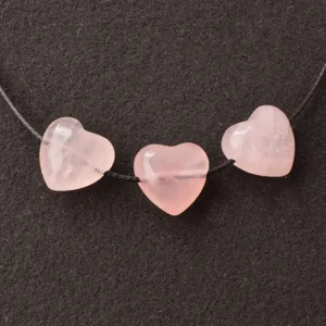 Gros plan de trois perles cœur en quartz rose naturel de 15 mm sur un cordon noir DIY