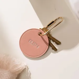 Gros plan sur un porte-clés rond en cuir rose avec gravure personnalisée et quincaillerie en laiton.