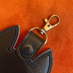Close-up detail shot of black PU leather cat ear keychain with durable metal lobster clasp.