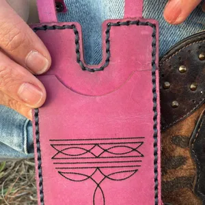 Primer plano detallado de tarjetero de cuero rosa con costuras negras y patrón geométrico.
