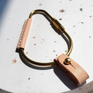 Close-up detail of brass carabiner keychain with PU leather wrap and metal rivet fastening.