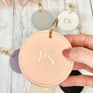 Round PU leather keychain detail, Saffiano texture, custom gold monogram initial charm tag.