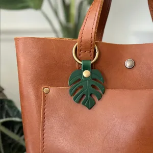 Close-up detail of green monstera leaf leather bag charm keychain pendant accessory.