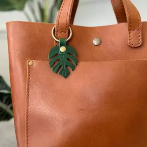 Close-up detail of green monstera leaf leather keychain bag charm hanging on vintage bag.