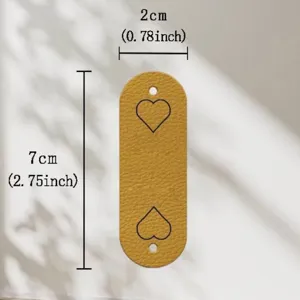 Close-up detail of the oval PU leather tag with laser engraved heart patterns and stitching holes.