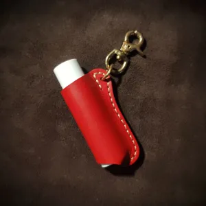 Gedetailleerd overzicht van rode lederen lippenstifthouder met messing sleutelhanger draagbaar.