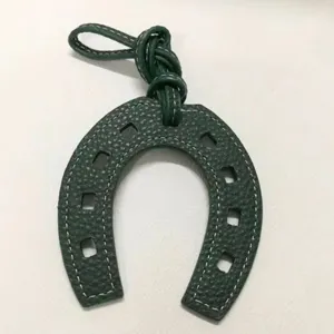 Detailed view of the green leather horseshoe bag charm with contrast white stitching and strap.