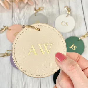 Close up detail of round PU leather keychain with gold foil monogram letter on wooden table.
