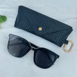 Close-up detail of black woven glasses case and stylish sunglasses with gold hardware.
