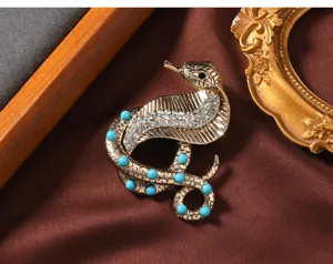 Close-up detail of a vintage gold-tone cobra brooch with turquoise beads and sparkling rhinestones.