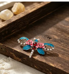 Gros plan d'une broche libellule en émail de style chinois avec des fleurs et strass.