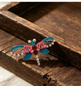 Détail de broche libellule style chinois, finition émail vintage avec perles et pierres rouges.