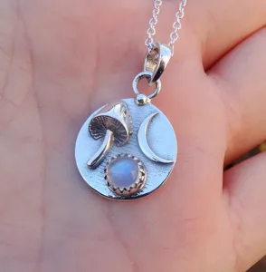 Close-up detail of silver necklace pendant featuring mushroom, crescent moon and moonstone.