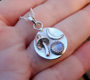 Close up detail of silver pendant necklace featuring cute mushroom moon and glowing moonstone.