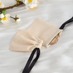 Vista dettagliata di sacchetti in cotone beige con nastri neri per confezioni di gioielli.