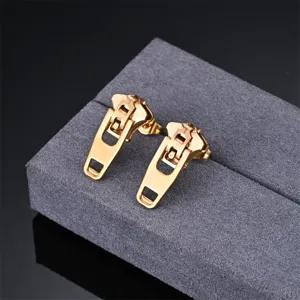 Detailed close-up shot of creative gold zipper-shaped stud earrings on grey velvet display.