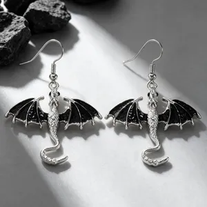 Close-up details of alloy dragon earrings with black enamel wings and silver hooks.