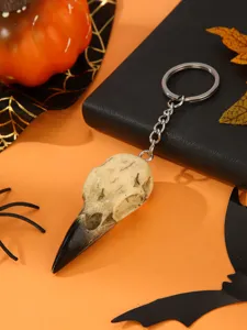 Detailed shot of a gothic bird skull keychain with metal ring on Halloween orange background.