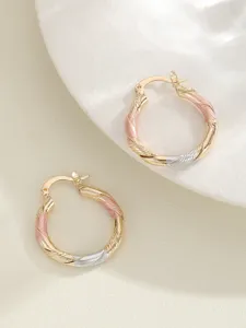 Close-up detail van stijlvolle driekleurige gedraaide creolen in goud, zilver en roze tonen.