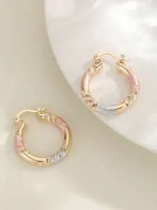 Gedetailleerde close-up van driekleurige gedraaide creolen oorbellen met gouden en zilveren tonen.