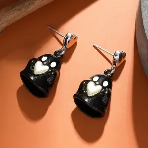 Dettaglio orecchini fantasma nero di Halloween con cuore dorato su sfondo arancione, primo piano.