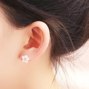 Close-up detail view of a sweet cherry blossom stud earring with pink center worn on ear.