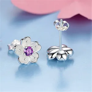Detailed view of silver cherry blossom stud earrings with purple center stone and fine frosted finish.