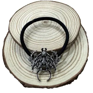 Detailansicht des Gothic Totenkopf Motten Haargummis mit Metallanhänger auf rüstikalem Holz.