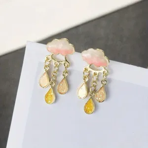 Close-up detail of cute cloud and teardrop enamel earrings, sweet pink and yellow design.