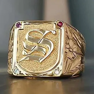 Gold signet ring detail showcasing Gothic letter S engraving, textured finish and floral side motifs.