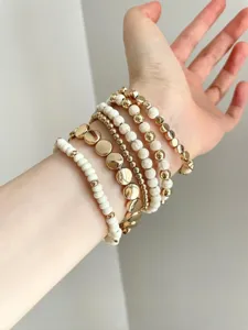 Detailed close-up of stacked bohemian gold and white beaded bracelets worn on wrist.