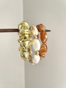 Detailed close-up of layered bohemian style bracelets featuring gold, white and amber beads.