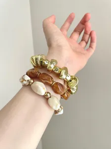 Close-up detail shot of stacked statement bracelets featuring irregular gold and resin beads.