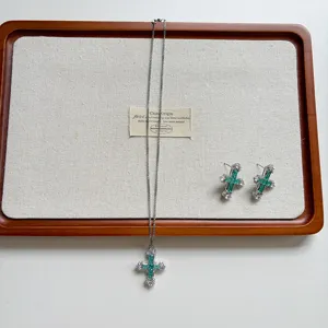Detailed close-up view of the sparkling emerald zircon cross necklace and earrings.
